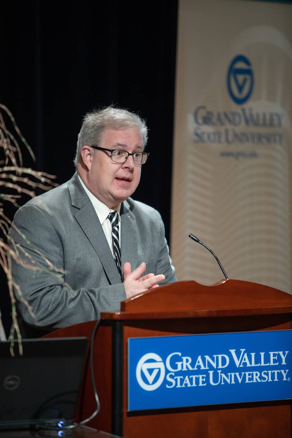 Man speaking at a GVSu podium, looking out into the audience